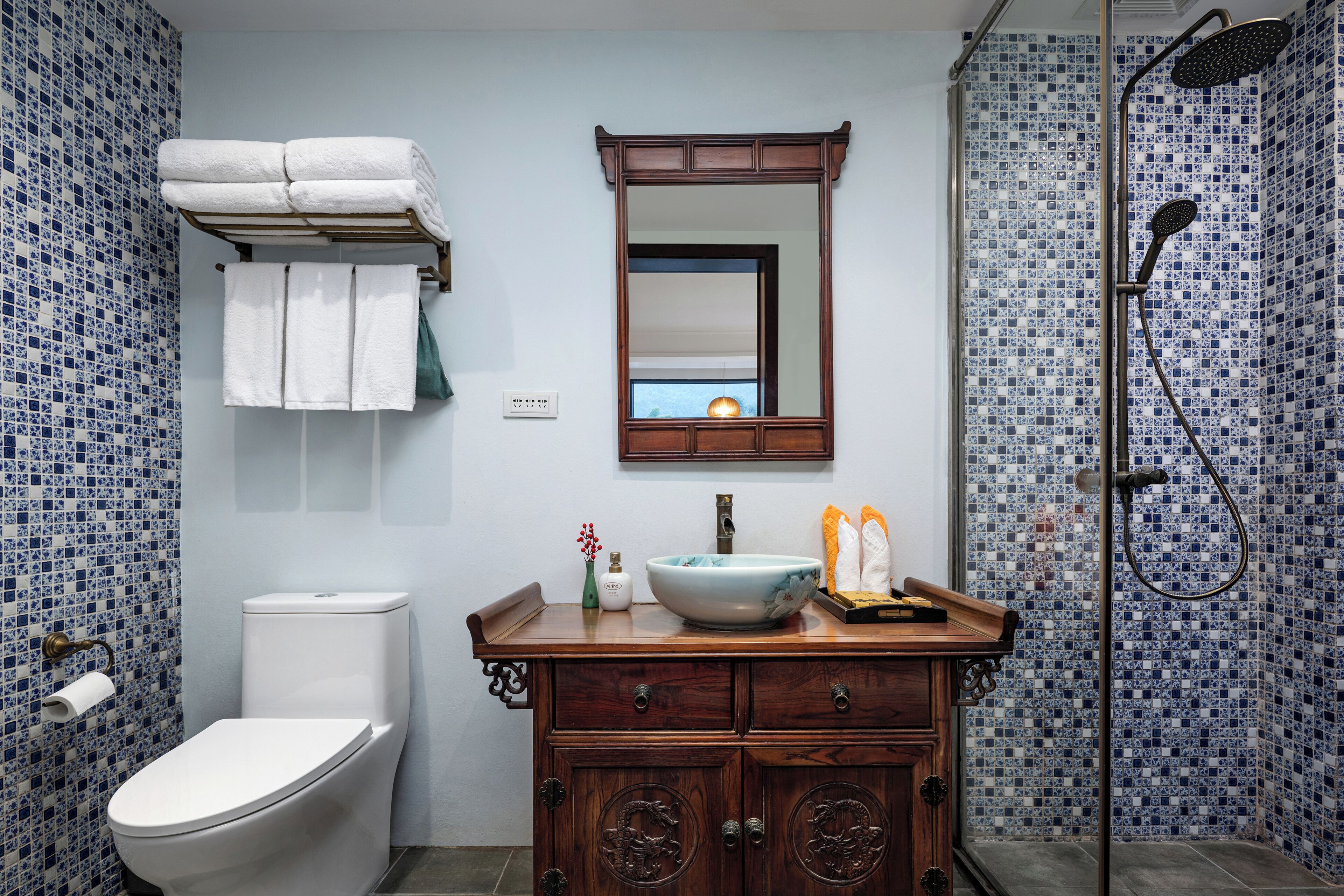 A bathroom with a toilet, a sink with a mirror above it, a shower area, and a towel rack with towels.