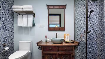 A bathroom with a toilet, a sink with a mirror above it, a shower area, and a towel rack with towels.