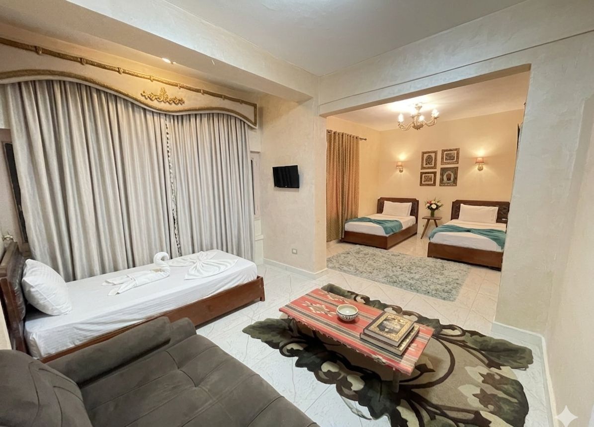 Hotelkamer met een bed, een slaapbank, een bijzettafeltje en zicht door een boog op een andere kamer met twee bedden.