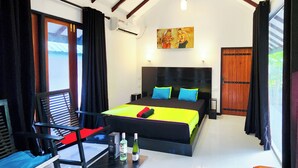 A bedroom with a bed, a chair, a table with bottles, a painting, and a window.