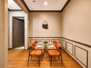 Comedor con una mesa lista para cuatro, rodeado de cuatro sillas naranjas, un espejo en la pared y suelo de madera.