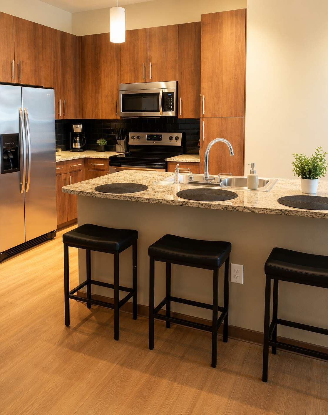 A modern kitchen with wooden cabinets, stainless steel appliances, a granite countertop, and three bar stools.