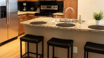 A modern kitchen with wooden cabinets, stainless steel appliances, a granite countertop, and three bar stools.