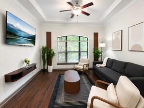 A living room with a TV, sofa, coffee table, and a window with blinds.