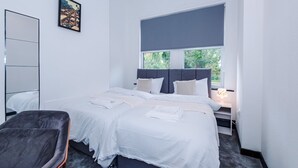 Un dormitorio moderno con una cama grande, una mesita de noche con lámpara, una silla y un cuadro en la pared.