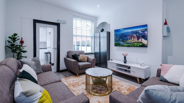 Una sala de estar moderna con un sofá, un sillón, una mesa de centro y un televisor de pantalla plana montado en la pared.