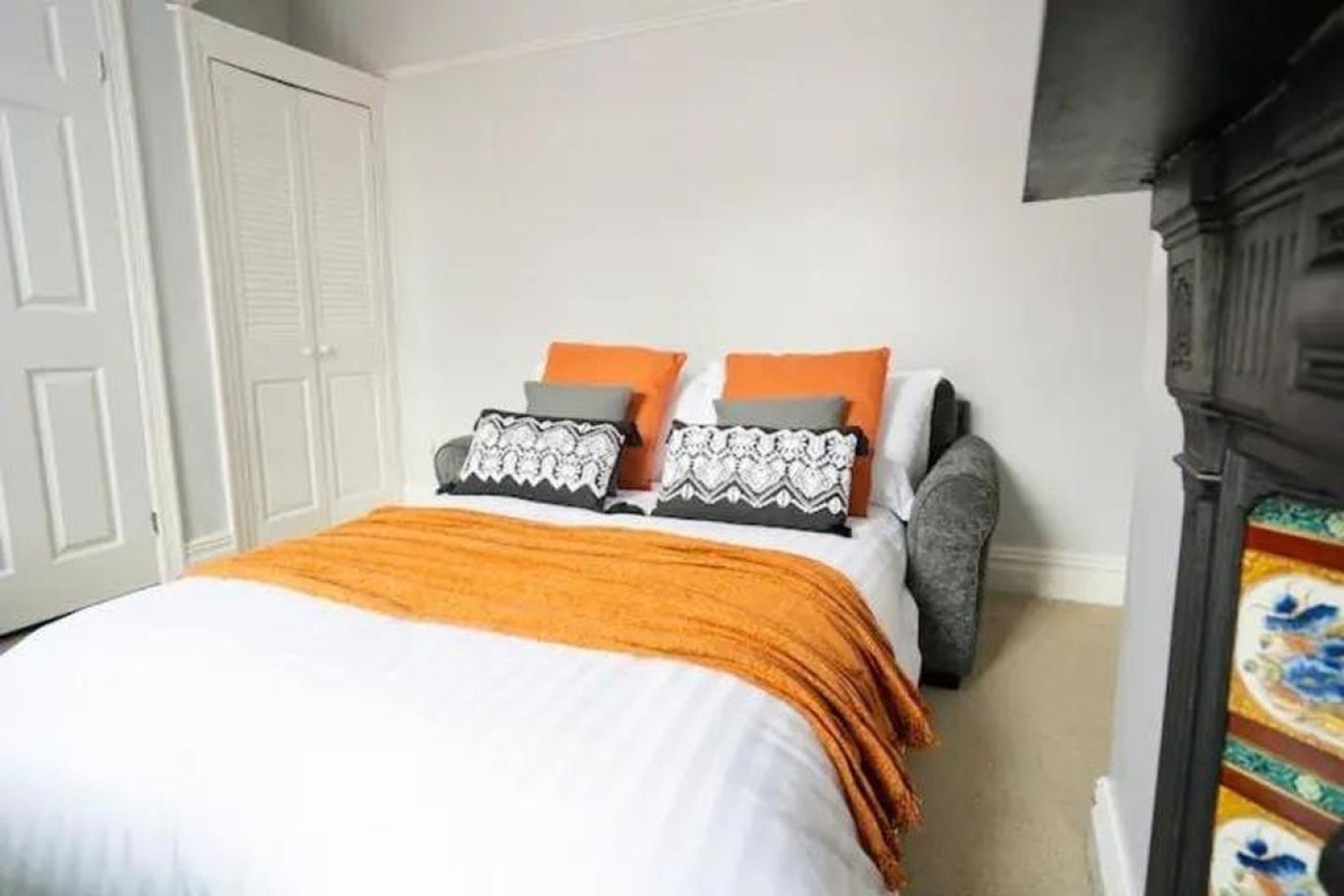 A bedroom with a bed, pillows, a blanket, a wardrobe, and a fireplace.