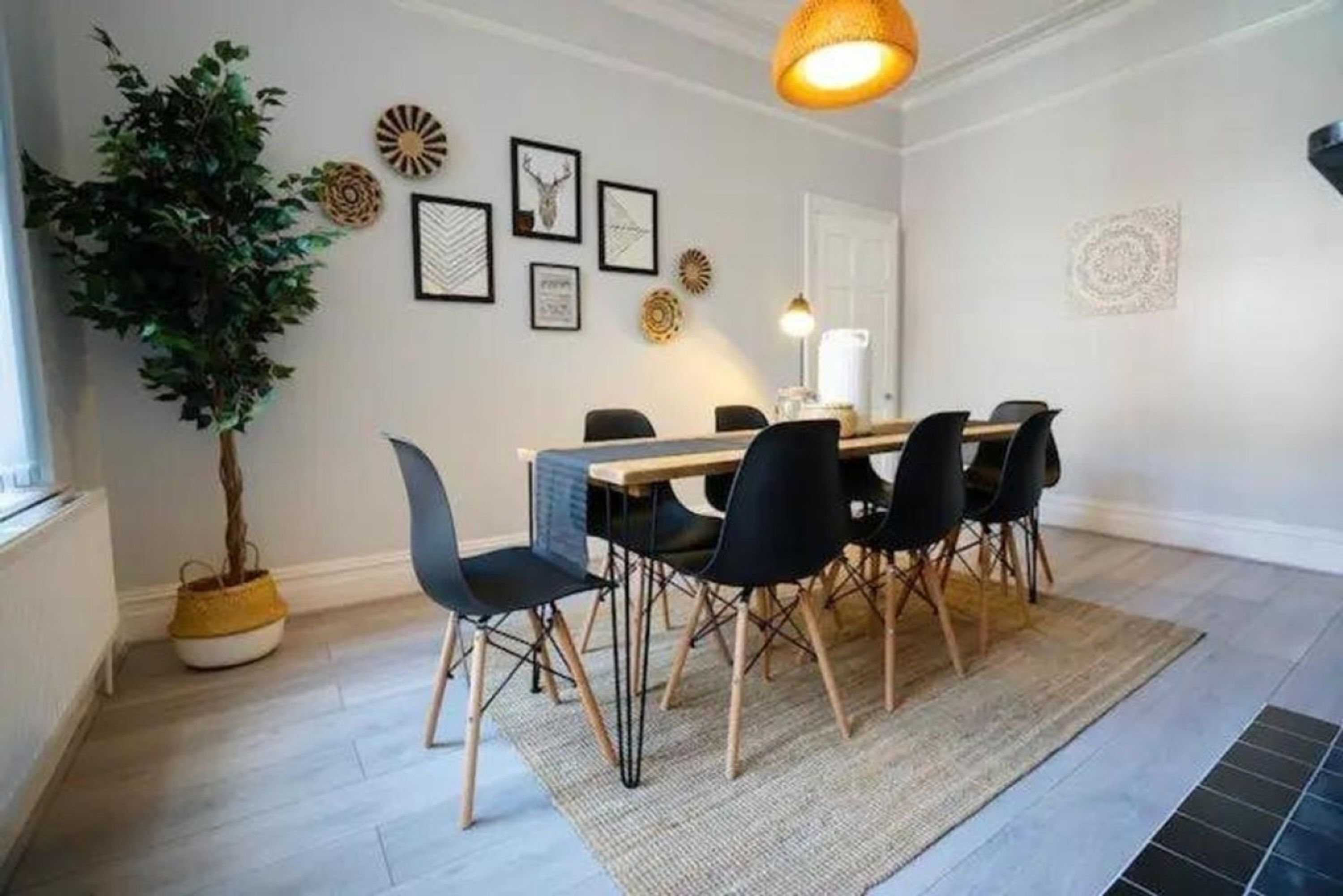 A dining area with a wooden table, black chairs, a potted plant, and wall decor.