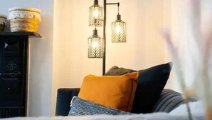 Ein Schlafzimmer mit einem Bett, einer schwarzen Kommode, einer Wandleuchte und einer Pflanze.