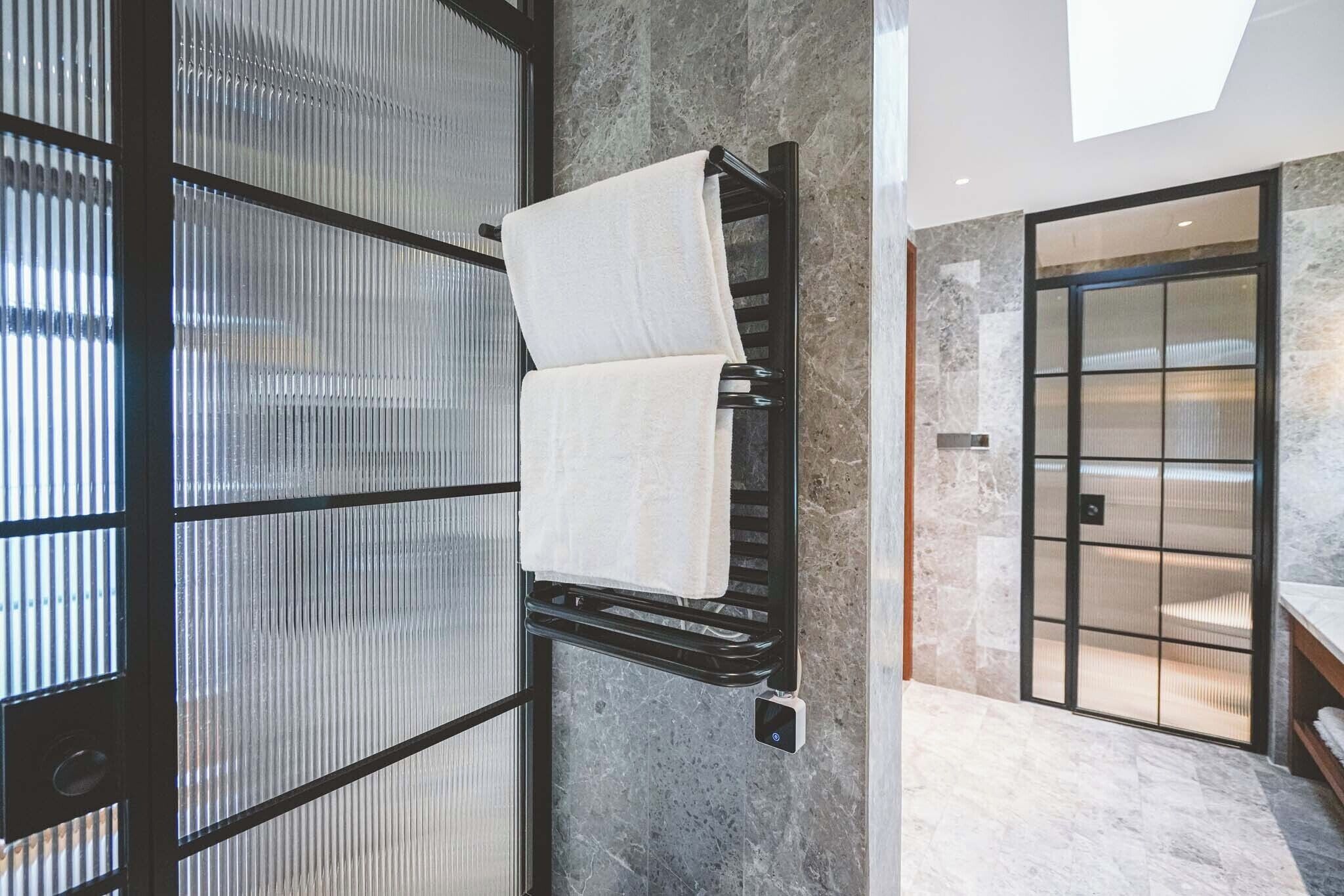 Un baño moderno con puerta de vidrio, un perchero con dos toallas y suelo de mármol.