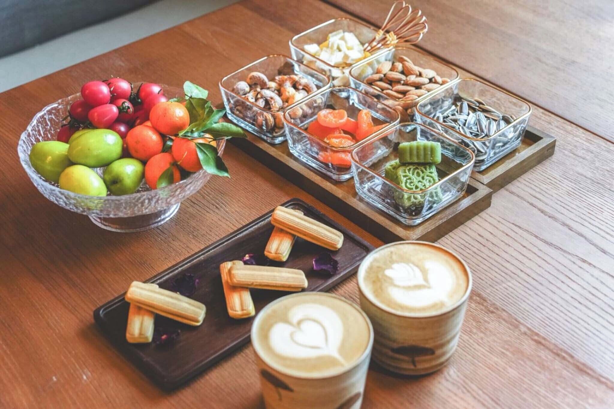 Ein Holztisch mit einer Schale Obst, einer Auswahl an Gebäck und zwei Tassen Kaffee.