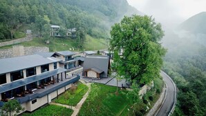 Um hotel moderno com telhado plano, grandes janelas e área de refeições com mesas ao ar livre.