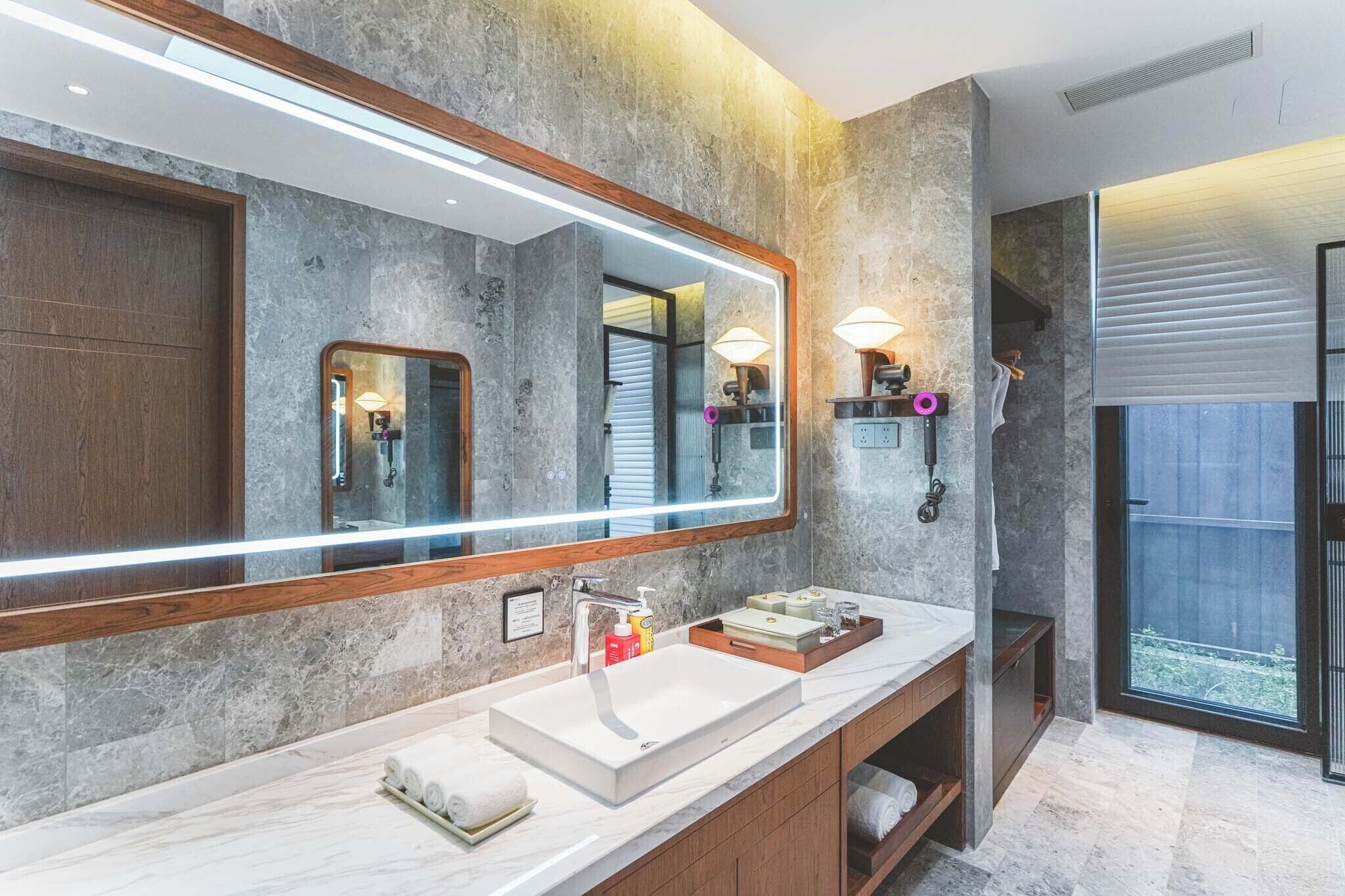 Un baño moderno con un espejo grande, un lavamanos blanco y un mueble de tocador de madera.