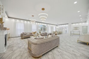 Ein geräumiges Wohnzimmer mit einem großen beigen Sofa, einem Kamin und einem Essbereich mit einer Chandelüster.