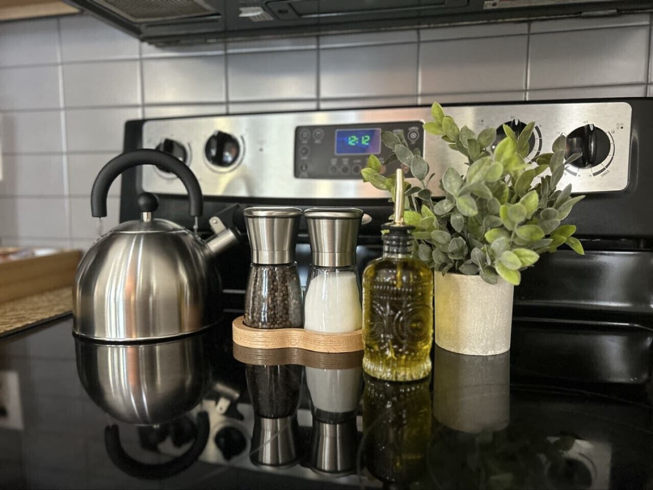 A kitchen with a stainless steel kettle, salt and pepper shakers, a bottle of oil, and a potted plant on a reflective countertop.