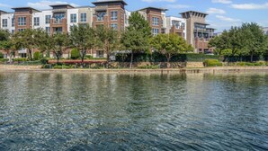 A waterfront hotel with modern architecture, a reflective pool, and a well-maintained garden.