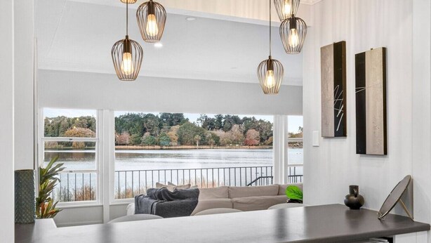 Una cocina moderna con un amplio ventanal con vistas a un lago, una zona de estar integrada y lámparas colgantes.