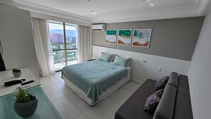 Ein modernes Schlafzimmer mit einem Bett, einem Sofa, einem kleinen Tisch mit einer Pflanze und Blick auf Gebäude durch das Fenster.
