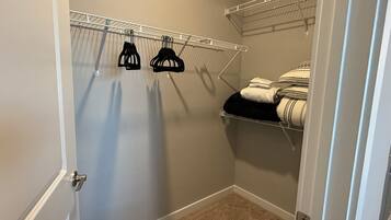 A closet with hanging storage and shelves, carpeted floor, and a door with a silver handle.