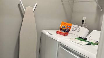 Un espace dédié à la lessive, équipé d’un sèche-linge, d’un fer à repasser et de produits de lessive.
