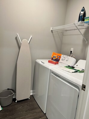 Un espace dédié à la lessive, équipé d’un sèche-linge, d’un fer à repasser et de produits de lessive.
