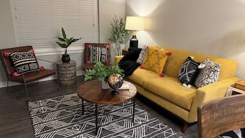 Un salon avec un fauteuil en cuir marron, un canapé jaune, une table basse ronde et un tapis à motifs.