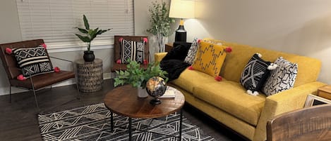 A living room with a brown leather chair, a yellow sofa, a round coffee table, and a patterned rug.