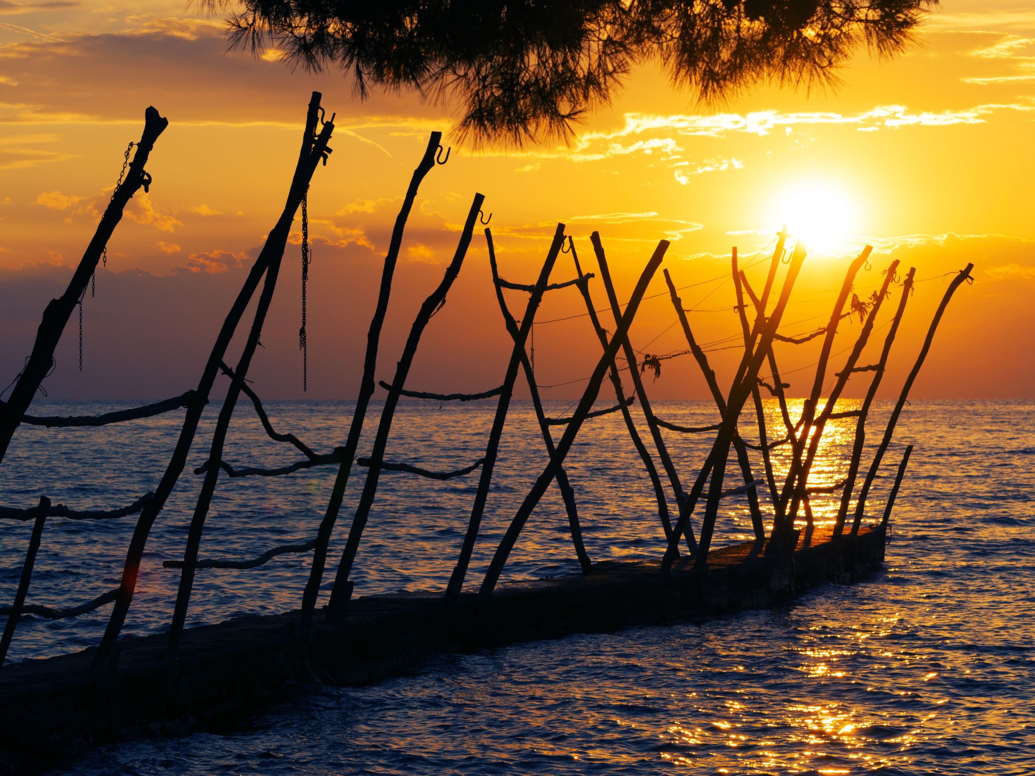 A sunset over the ocean with a wooden structure silhouetted against the sky.