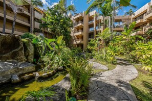 A hotel courtyard with a water feature, palm trees, and a stone pathway. - Ocean-view 2BR/2BA condo with pool, hot tub & beach access-Paki Maui 304 (Lahaina)