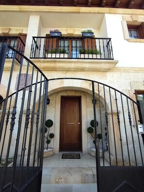 A two-story building with a wooden door, a balcony with potted plants, and a wrought iron gate.