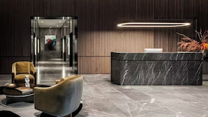 En moderne lobby med en receptionsdisk, et siddeområde med sofa og lænestol, samt en gang der fører til andre dele af bygningen.