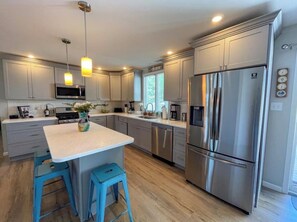 A modern kitchen with stainless steel appliances, a central island with stools, and a welcoming sign.