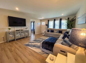 A modern living room with a flat-screen TV, a sofa, a coffee table, and a patterned rug.