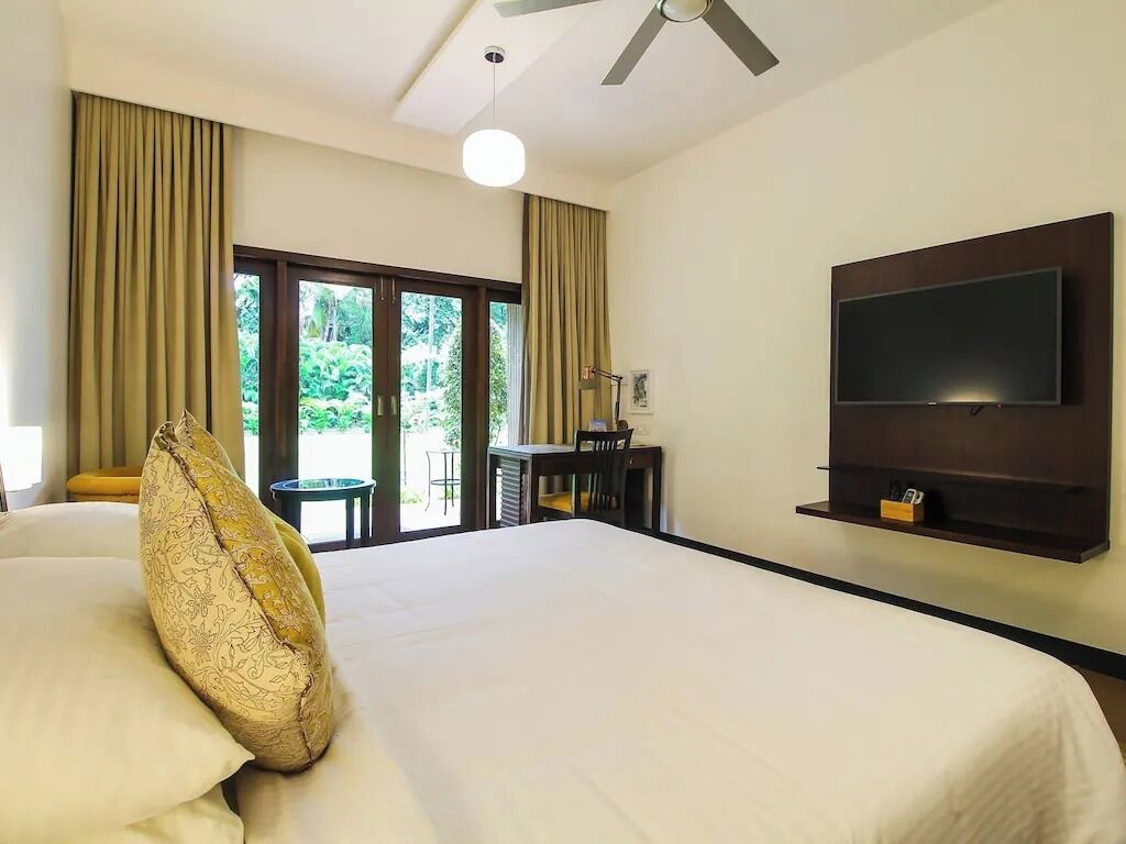 Habitación de hotel con una cama grande, un televisor de pantalla plana en la pared y vistas al exterior con zonas verdes.