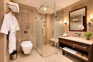 Un baño moderno con ducha envuelta en vidrio, inodoro blanco, tocador con espejo y toallero con bata blanca.