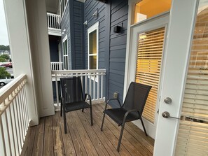 Eine Holzterrasse mit zwei Stühlen, einem weißen Geländer und einer Tür mit Rollläden.