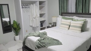 Ein Schlafzimmer mit Bett, Deckenventilator, Kleiderschrank, Spiegel und einer Zimmerpflanze.