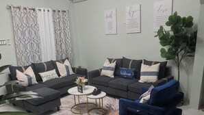 Ein Wohnzimmer mit einem Ecksofa, einem blauen Sessel, einem Couchtisch und einer Pflanze.
