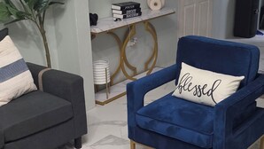 Ein modernes Wohnzimmer mit einem blauen Sessel, einem dunklen Sofa, einem runden Couchtisch und einem Schild mit der Aufschrift 'Willkommen bei Airbnb'.