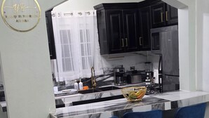 Eine moderne Küche mit schwarzen Schränken, einer Marmorarbeitsplatte und einem eingebauten Kühlschrank. Zwei blaue Barhocker mit goldfarbenen Beinen sind vorhanden.