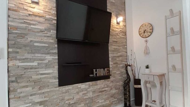 Un salon moderne avec un mur en pierre, un téléviseur fixé au mur, une horloge et un meuble blanc.