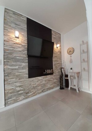 Ein modernes Wohnzimmer mit einer Steinwand, einem Wand-Fernseher, einer Uhr und einem weißen Schrank.