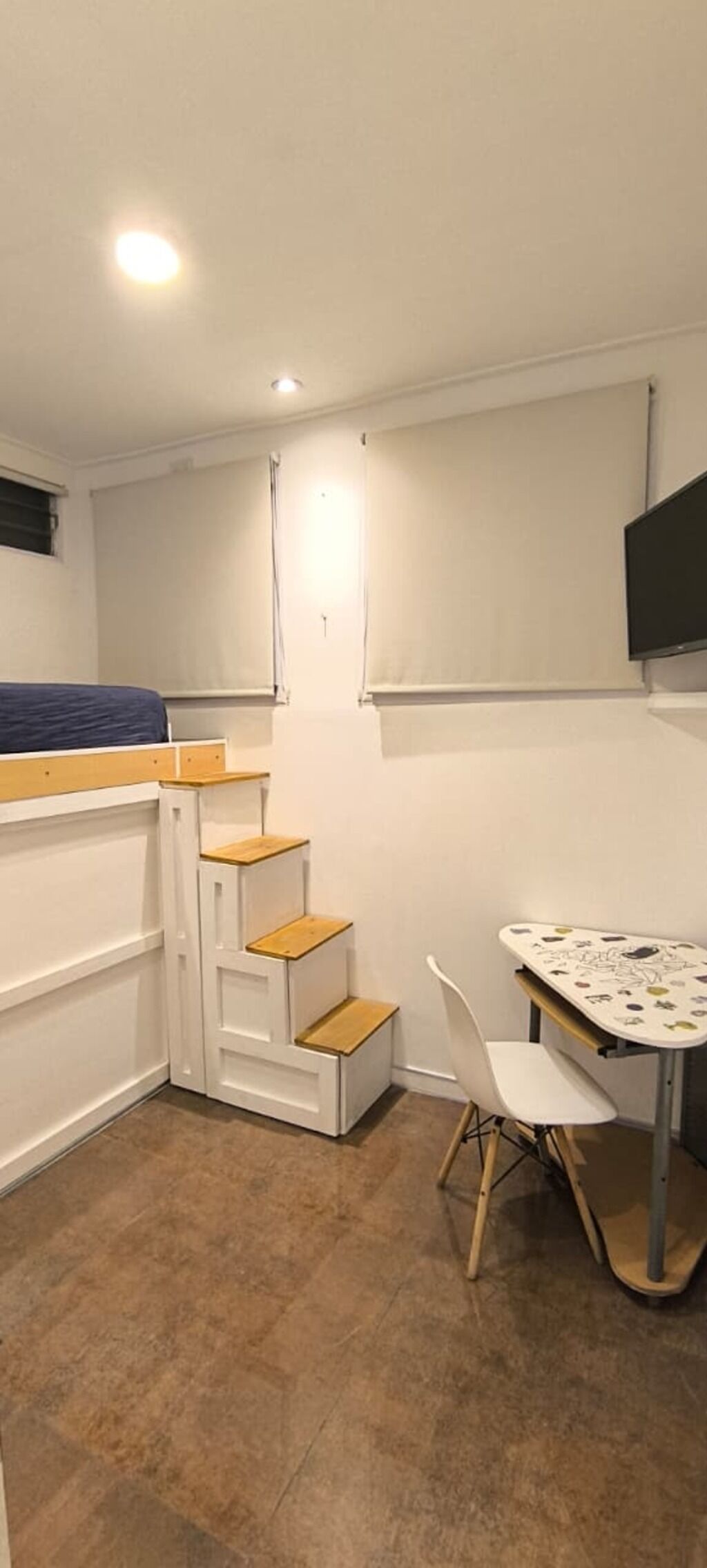 Een kleine kamer met een bed, een bureau, een stoel en een televisie die aan de muur is bevestigd.