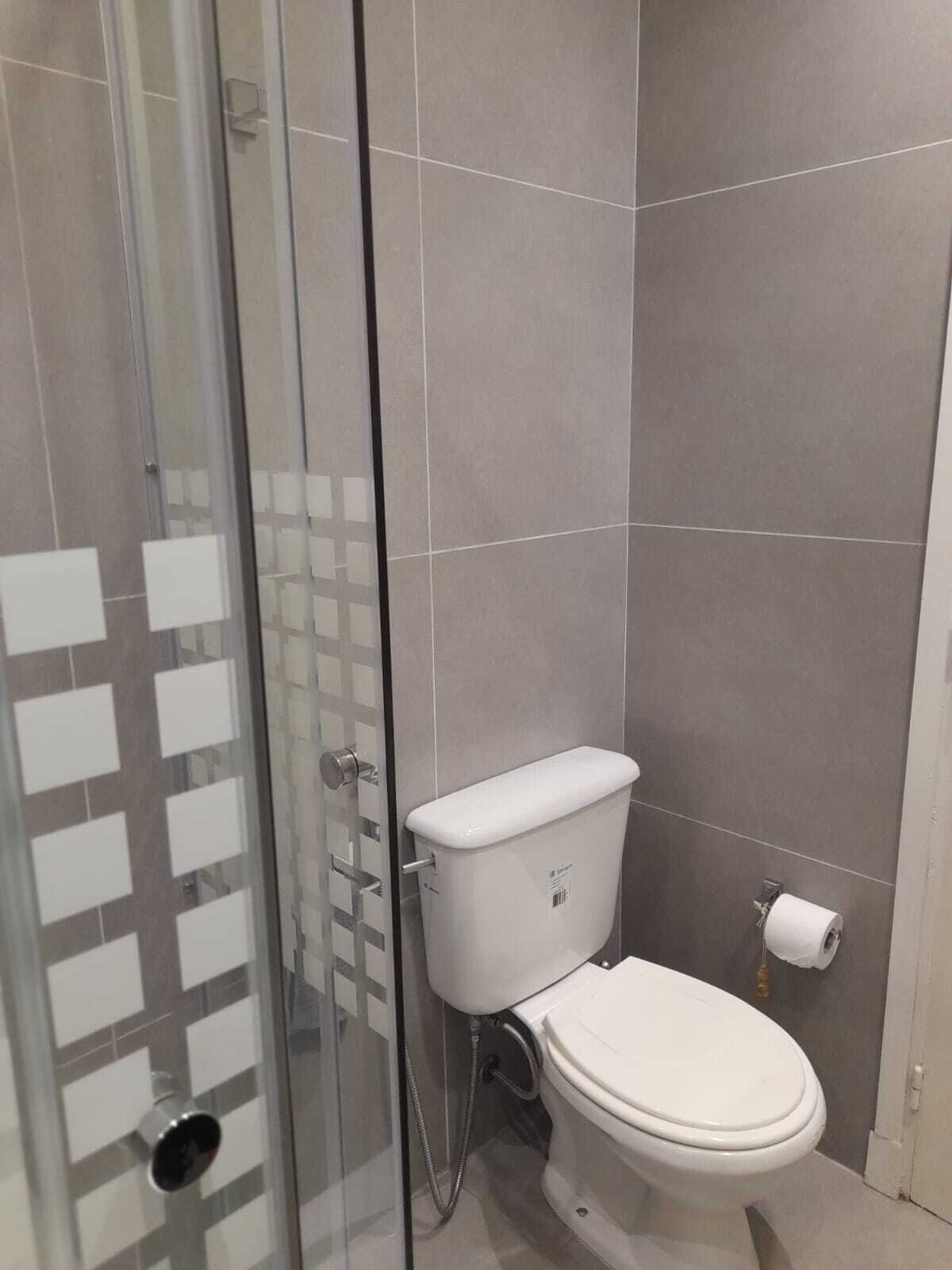 Une salle de bain moderne avec une douche à parois de verre, des toilettes blanches et un porte-rouleau de papier toilette apparent.