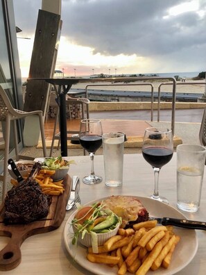 Ein Tisch mit einer Mahlzeit, darunter Steak, Pommes und Salat, sowie zwei Gläsern Rotwein.