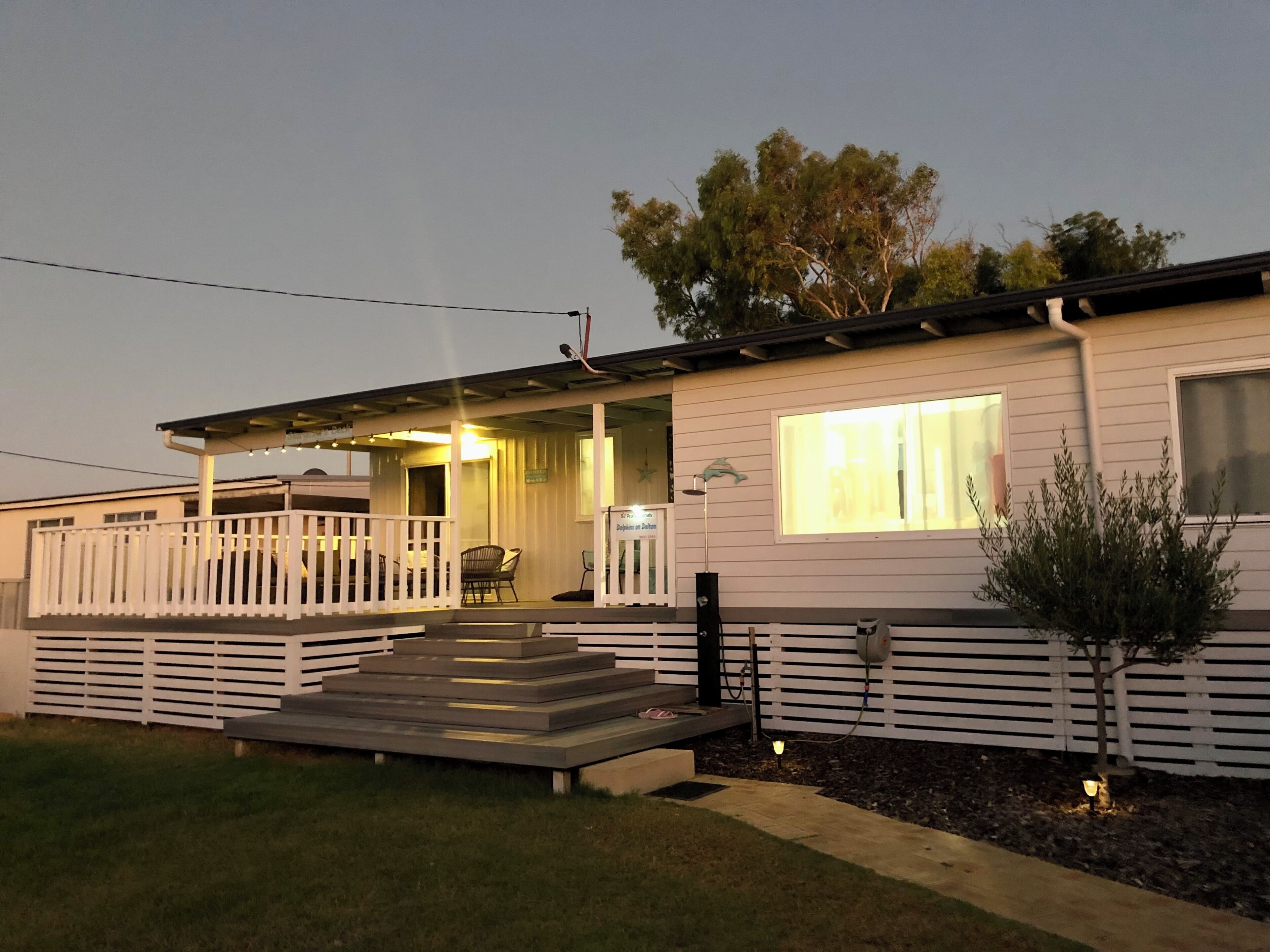 Uma casa térrea com varanda, um pequeno deck e um jardim frontal.