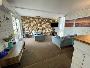 Ein Wohnzimmer mit Steinsandsteinwand, einem Flachbildfernseher, einem Sofa, einem Couchtisch und einer Holzbank.