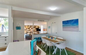 Ein modernes Zimmer mit Esstisch, weißen Stühlen, Fernseher und einer Steinwand.