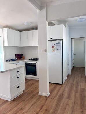 Eine moderne Küche mit weißen Schränken, einem Einbauofen, einem Kühlschrank und Holzboden.