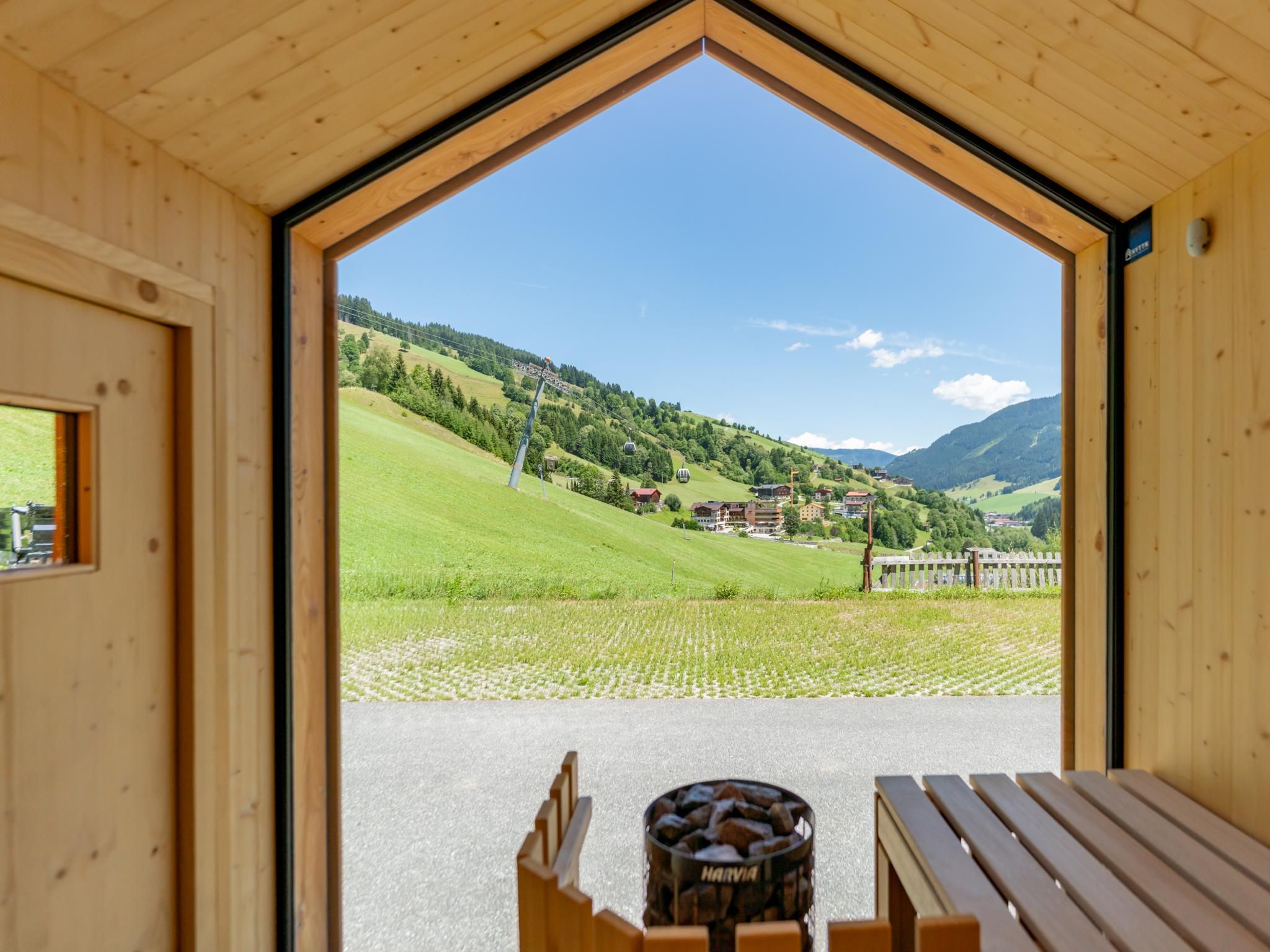 A wooden interior with a large window revealing a mountainous landscape, a bench, and a barrel labeled 'HARVIA'.